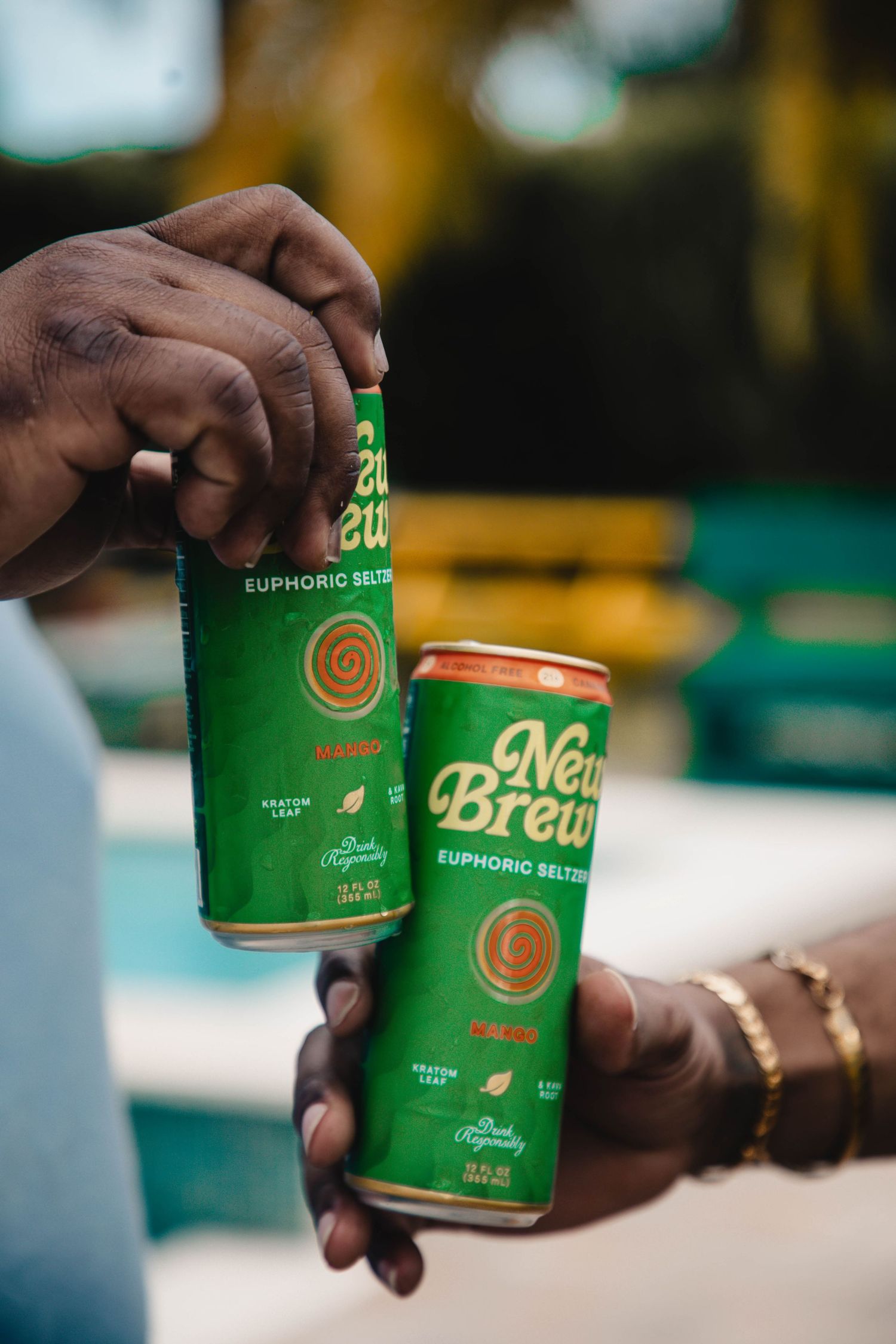 Hands holding green New Brew euphoric seltzer cans in outdoor setting.
