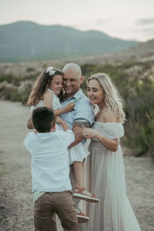 Happy family of four sharing a joyful moment outdoors with mountains in the background at sunset.