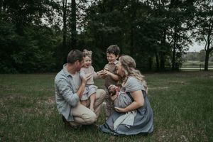 Family of four crouching together in a grassy field surrounded by lush green trees during an outdoor photo session.