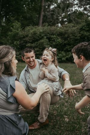 Happy family with two children laughing together outdoors in a lush green park setting.