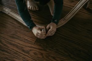 Child kneeling on hardwood floor holding a small object in their hands.