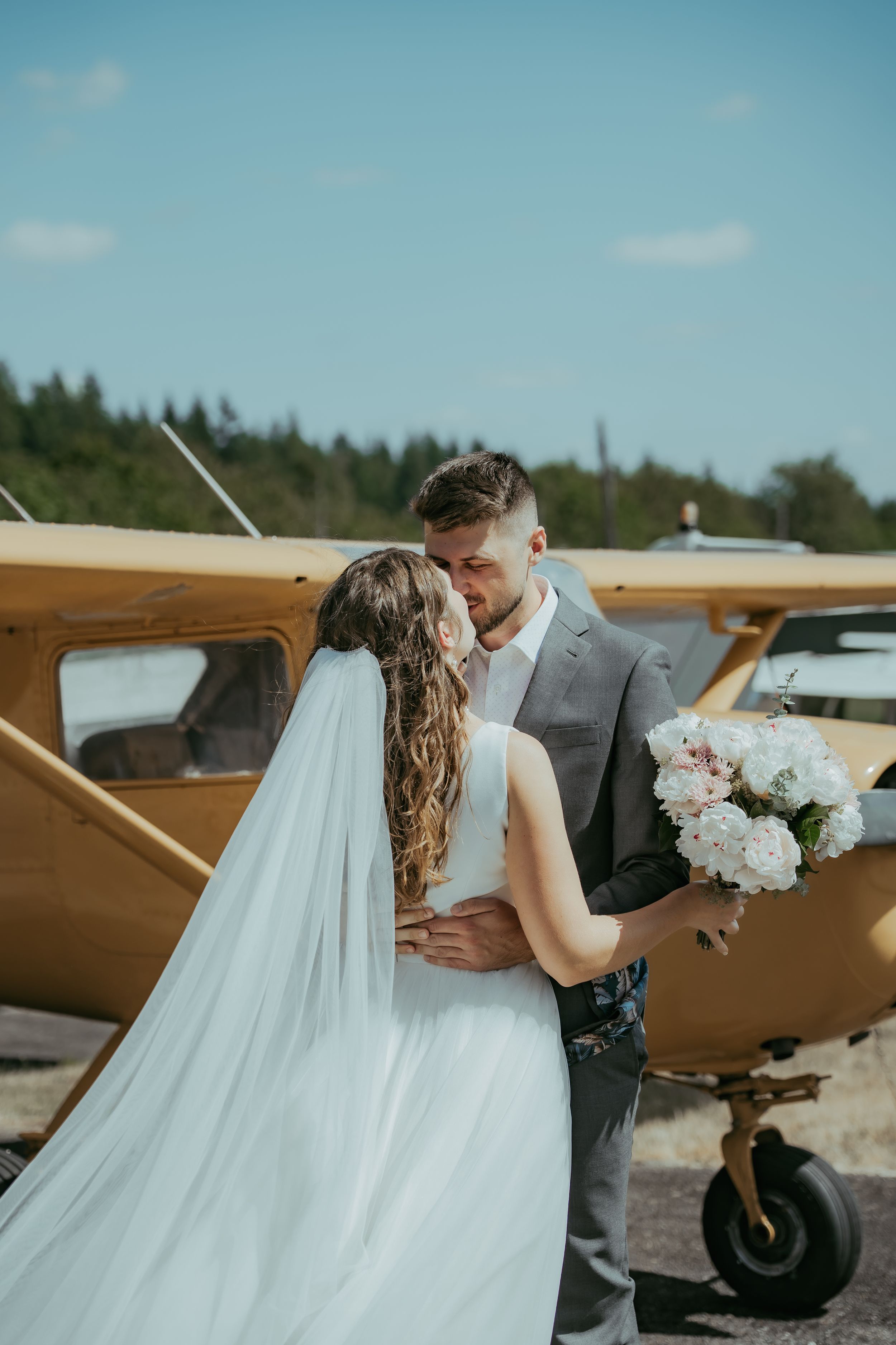 Bride and groom sharing a romantic kiss near a vintage yellow airplane on their wedding day.
