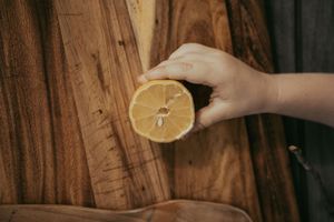 Hand holding a halved lemon over rustic wooden cutting boards, showcasing fresh citrus fruit texture.