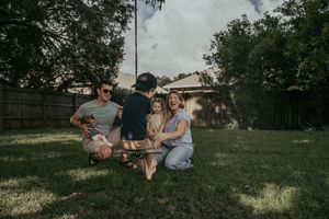 Happy family of four playing together on green grass in a backyard.