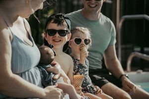Family with three children enjoying ice cream cones together outdoors on a sunny day.