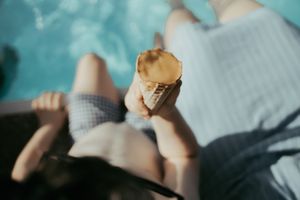 Child holding melting ice cream cone while sitting poolside on a sunny summer day.