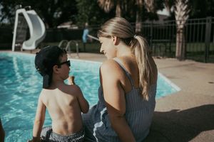 Mother and young son sitting together by a swimming pool on a sunny day.