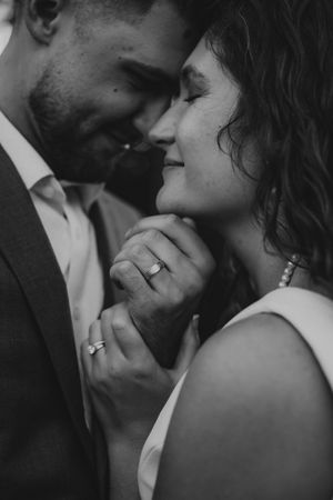 Black and white photo of a couple sharing an intimate moment, showcasing their wedding rings as they lean in for a kiss.