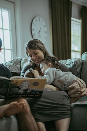 Smiling mother reading Blueberries for Sal book to young child on cozy sofa.