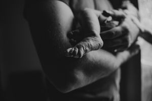 Black and white close-up of a newborn baby being cradled in adult arms during an intimate portrait session.