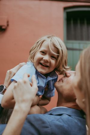 A delighted blonde toddler laughs while being held up by his father during a playful family photo session.