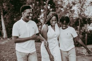 Joyful Black mother walking with two teenage sons in white outfits outdoors.