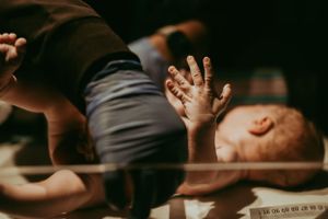 Newborn baby lying in hospital bassinet with tiny hand outstretched while parent reaches over.