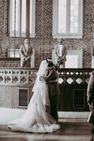 Black and white photo of bride and groom sharing their first kiss at a rustic brick church altar.
