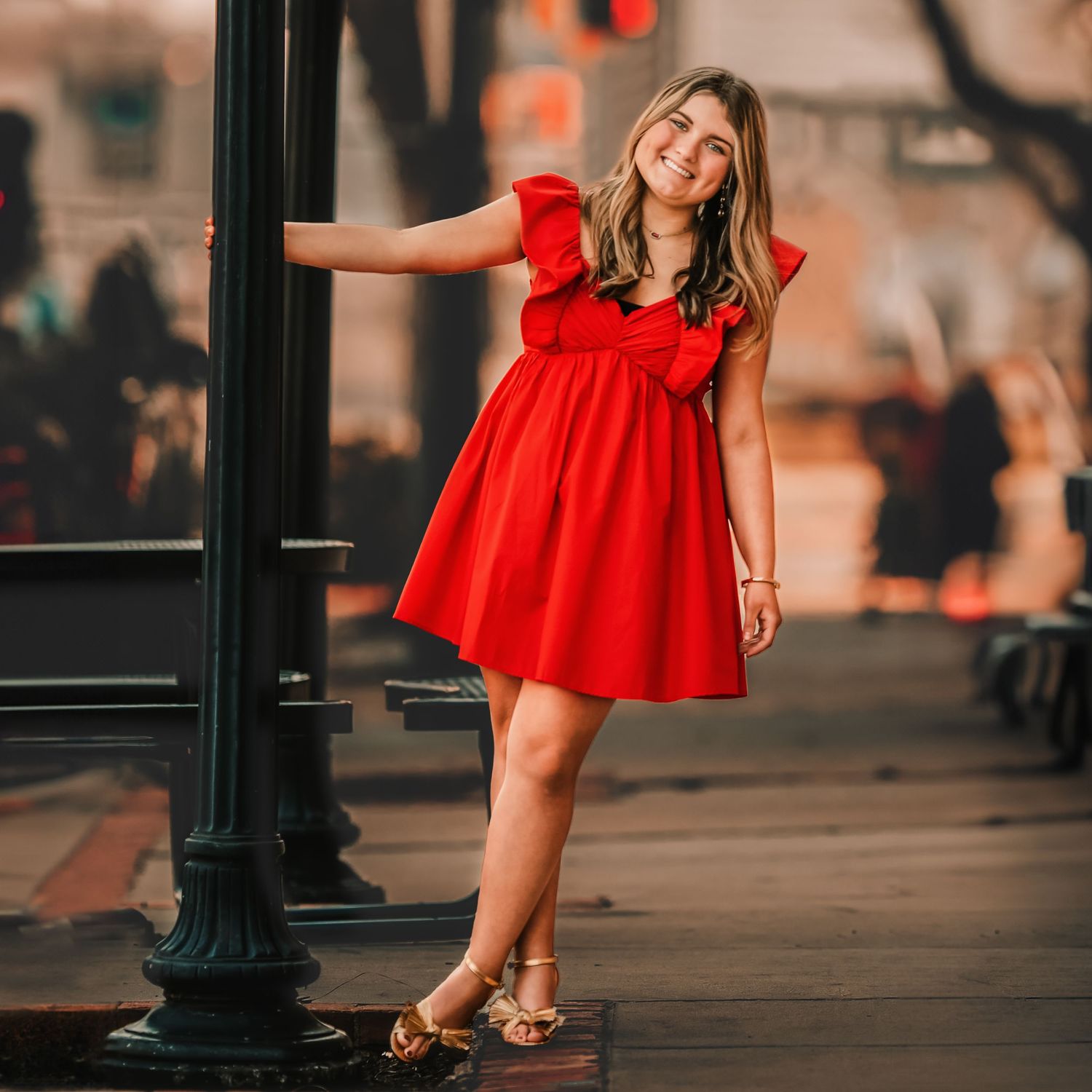 Flowing red dress twirls against urban backdrop with vintage lampposts.