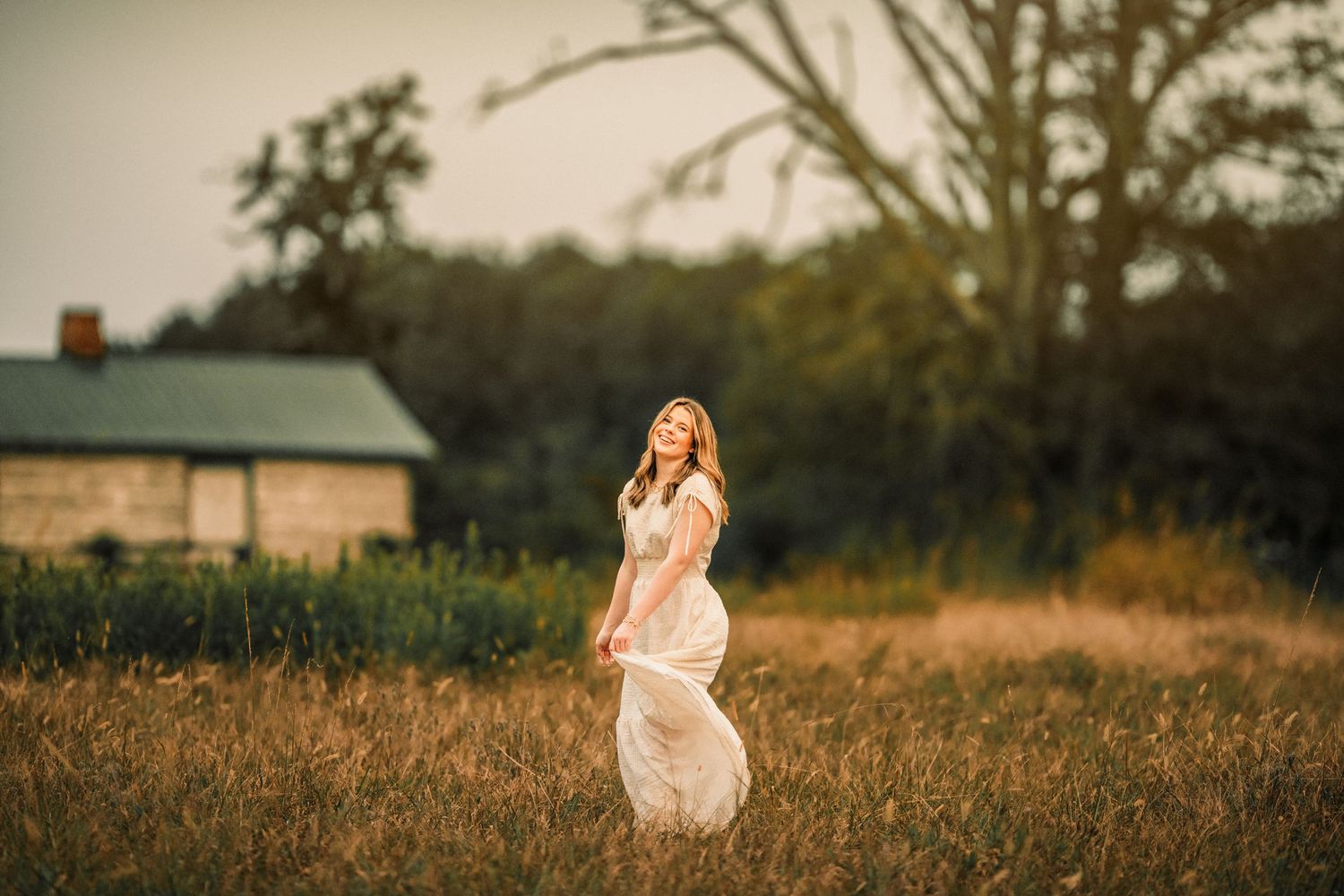 Ethereal sunset senior photoshoot in a golden field with flowing dress and natural lighting.