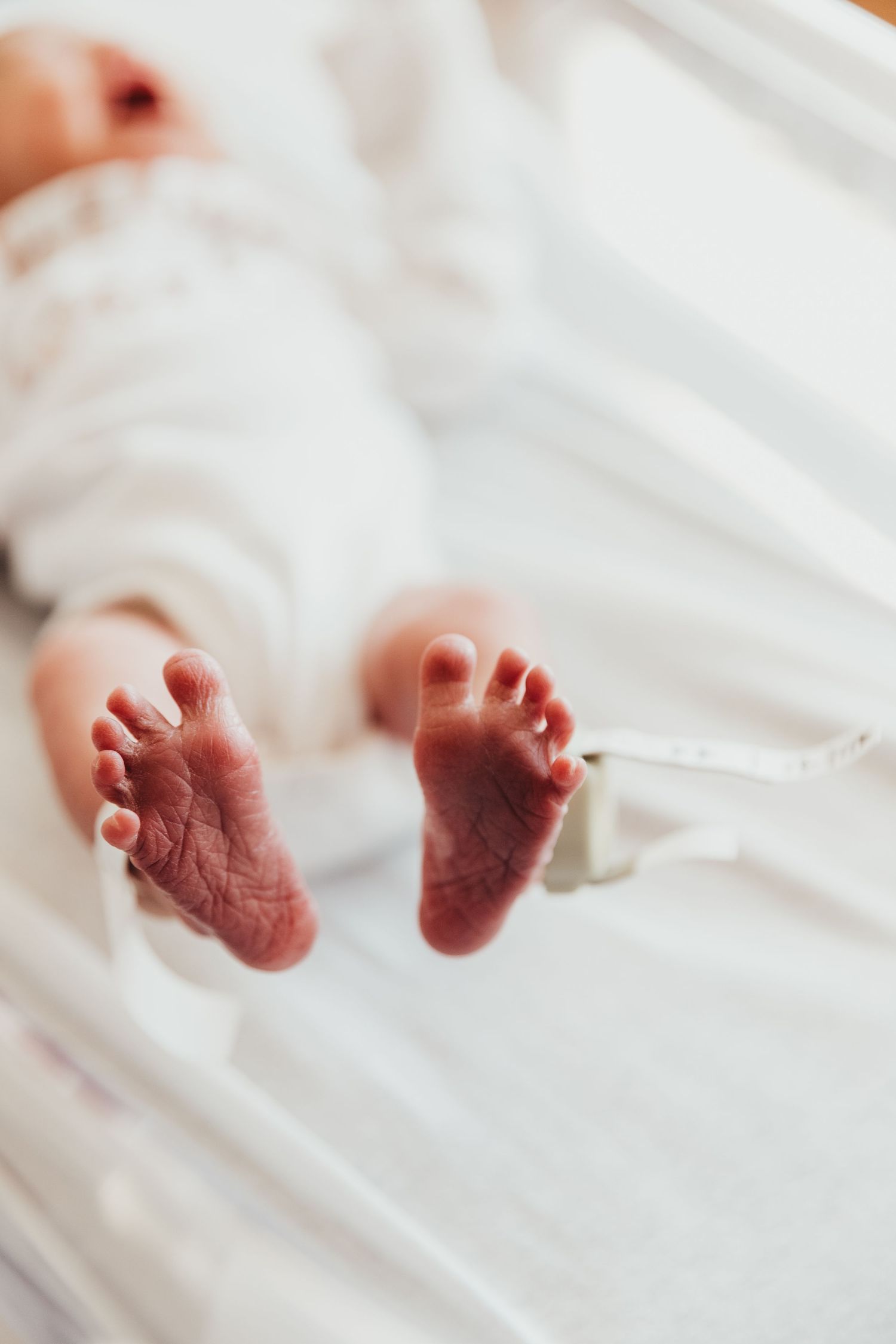 Close-up of tiny newborn baby feet against white bedding.