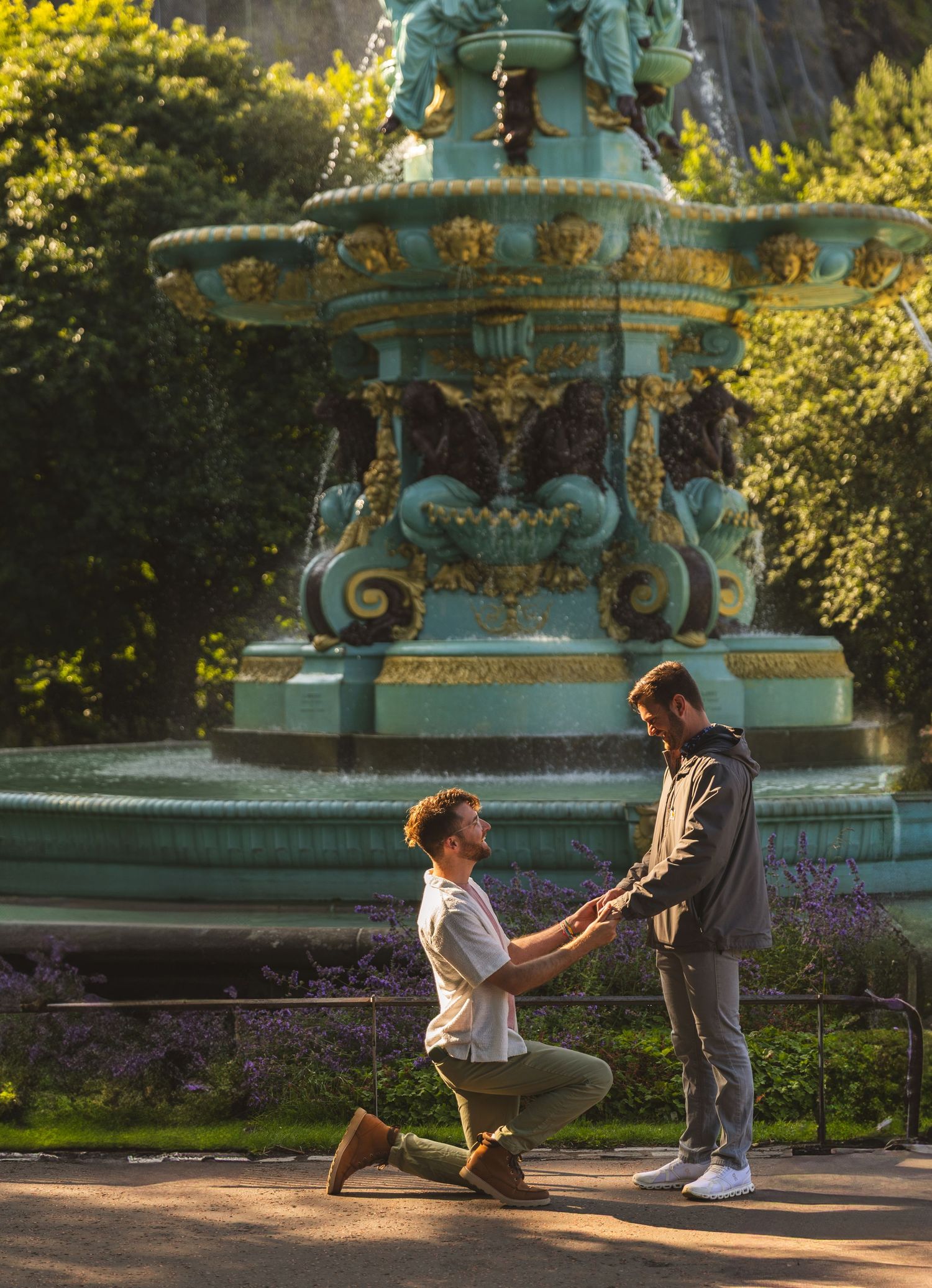 Surprise proposal moment captured in front of an ornate vintage fountain at sunset.