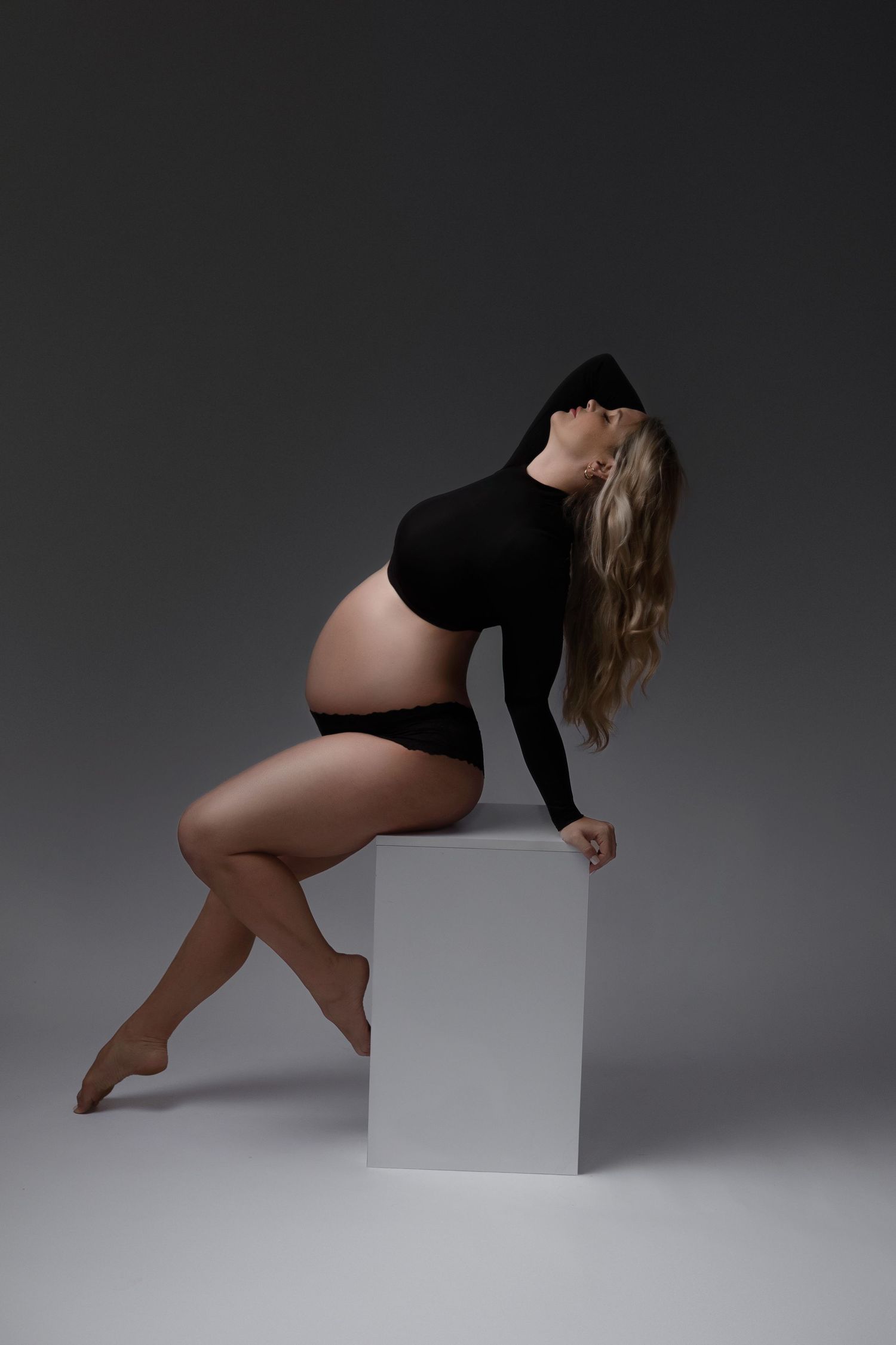 Artistic maternity silhouette against dark background shows expectant mother.
