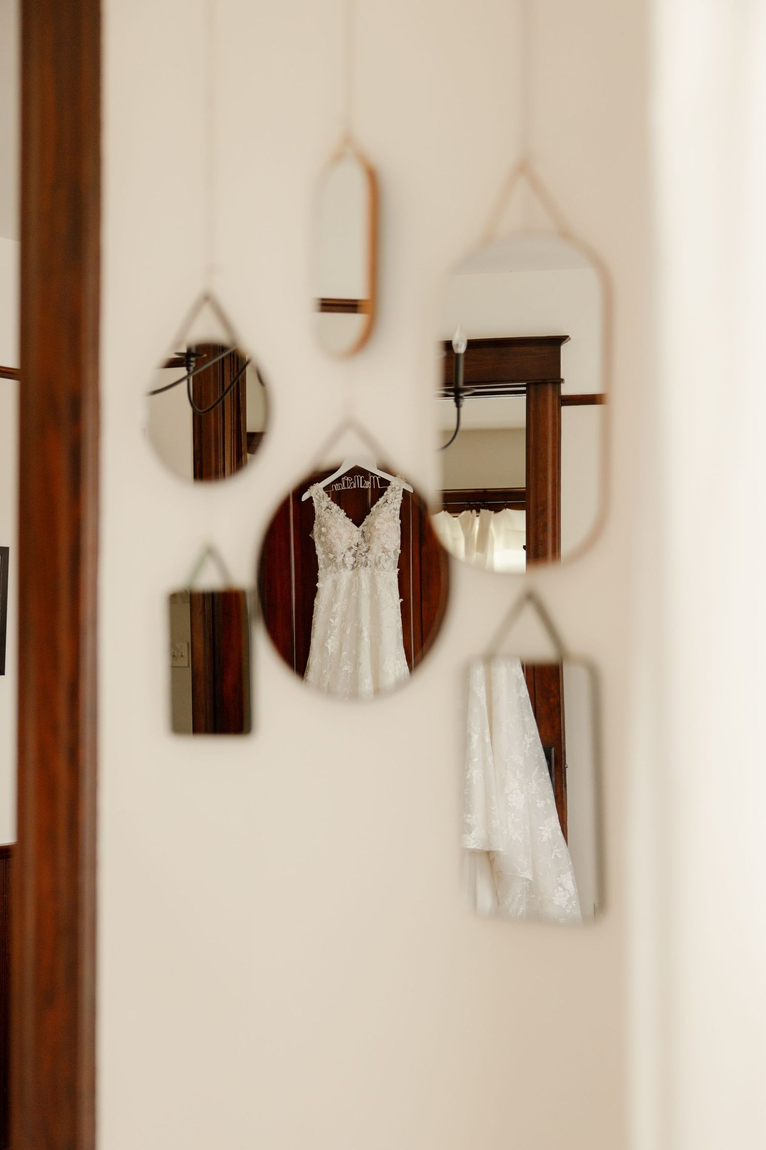 Wedding dress displayed among artistic mirrors on a white wall.
