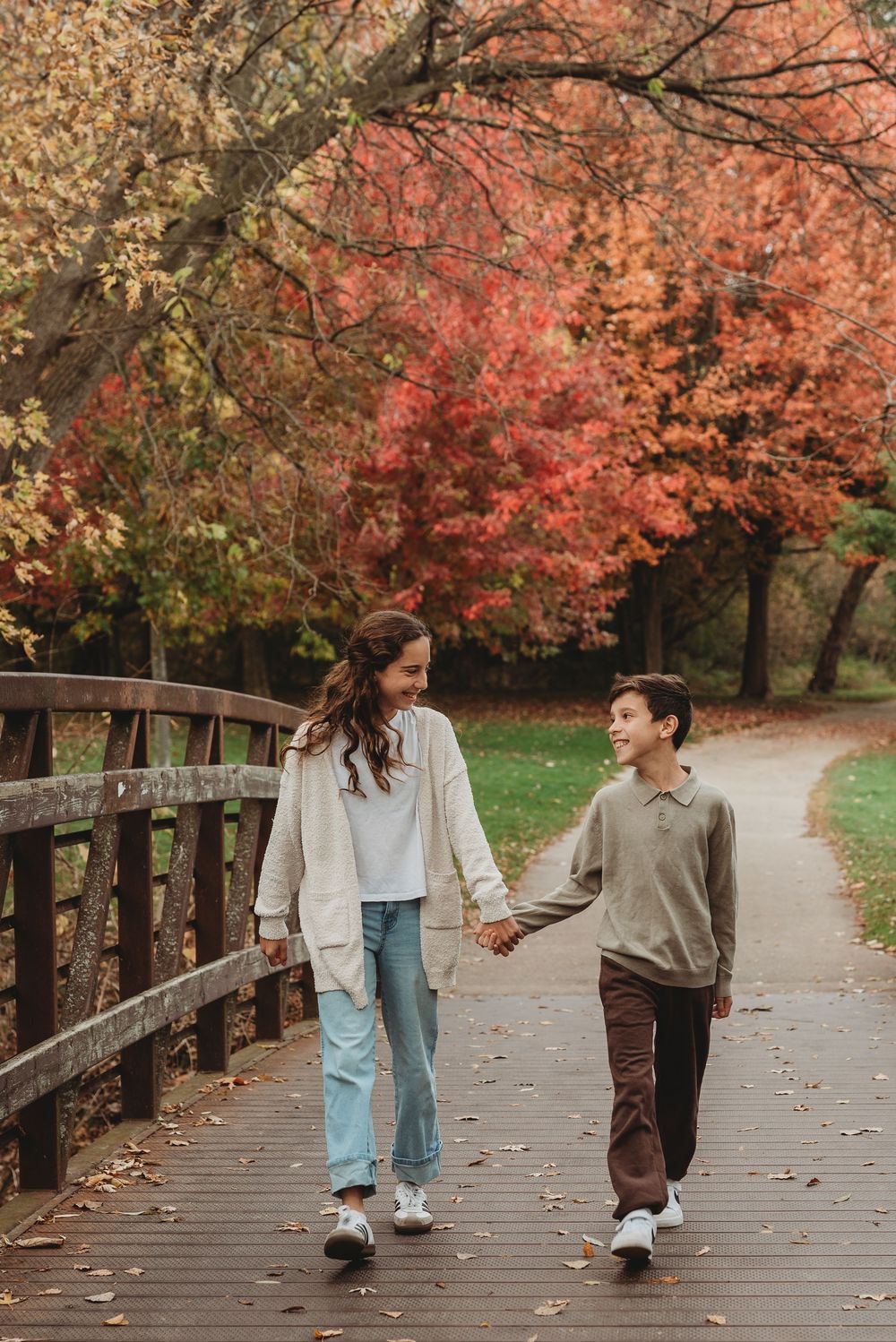 Siblings walking on bridge holding hands and smiling at each other during fall family outdoor session in Etobicoke