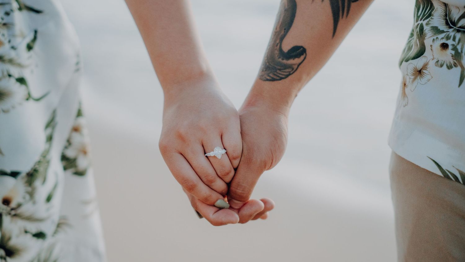 Close-up of tattooed hands holding together with engagement ring.