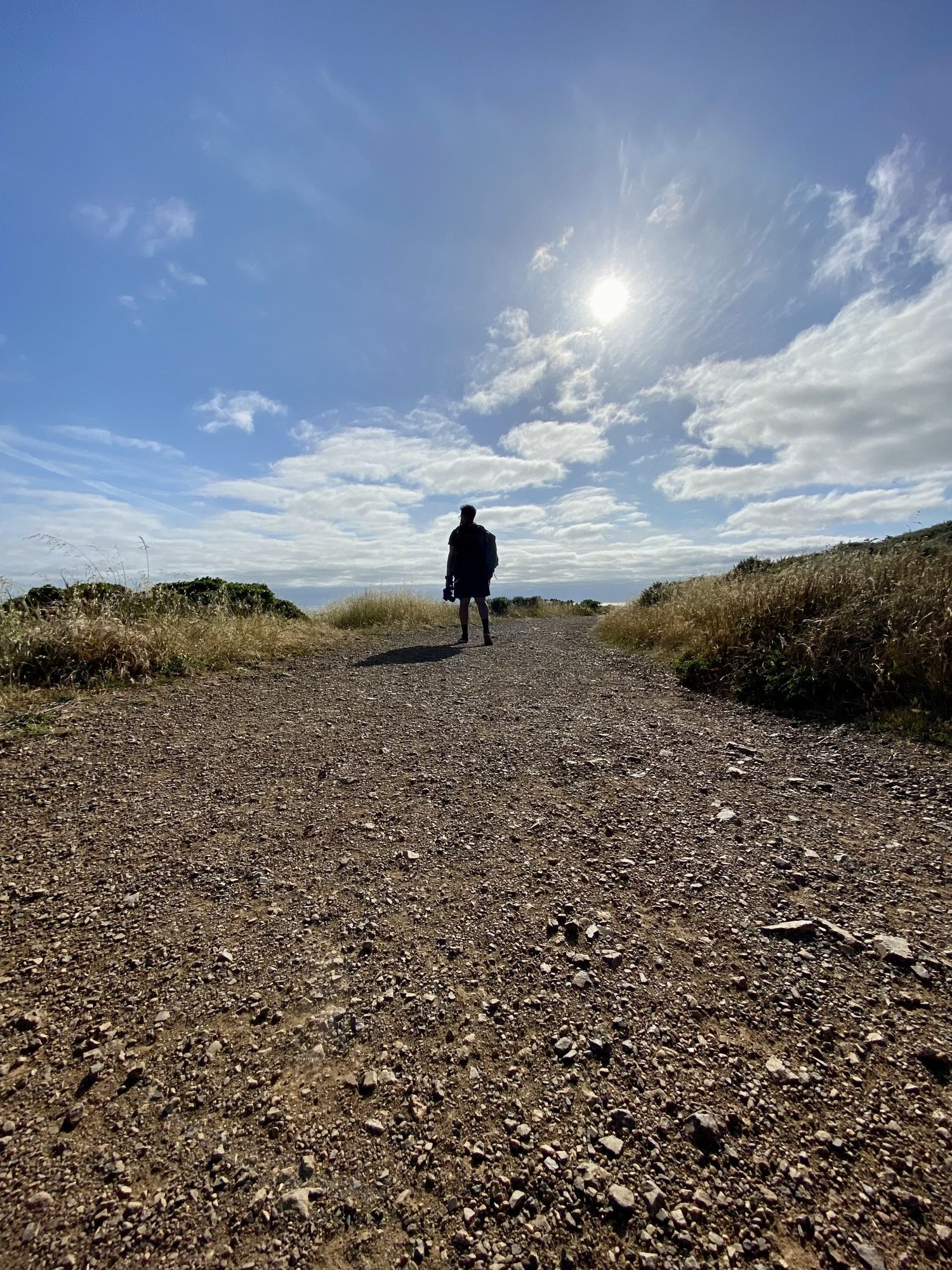 Solitary figure walking on dirt path under dramatic cloudy sky with sun beam.