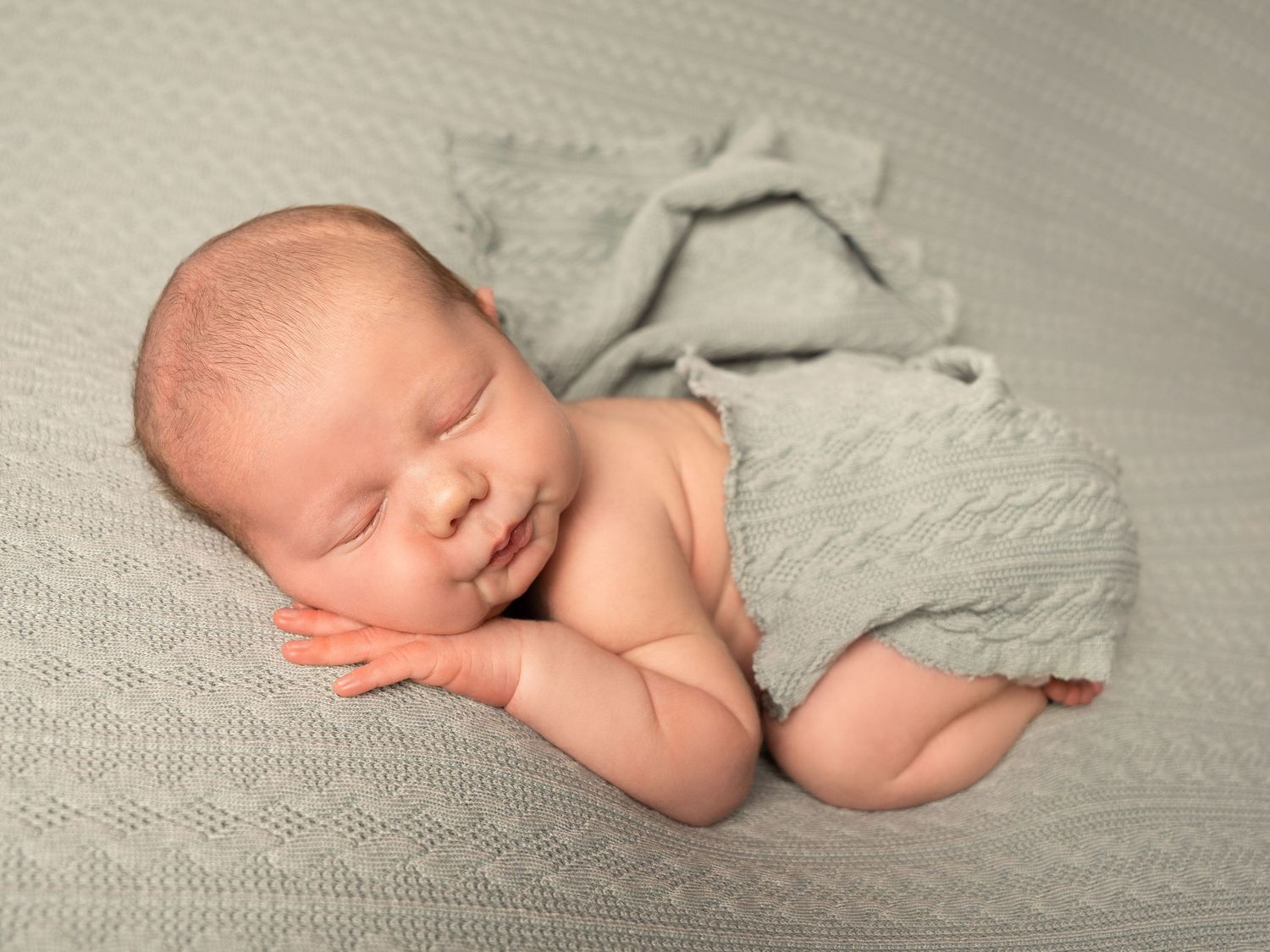 Baby boy sleeping on belly, posed on sage green textured blanket with draped wrap at newborn photoshoot in Doncaster.