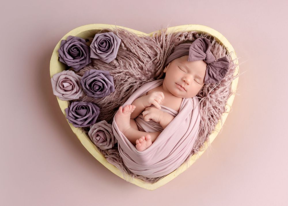 A series of newborn photography portraits with purple roses and soft pink fabric in heart-shaped frames.