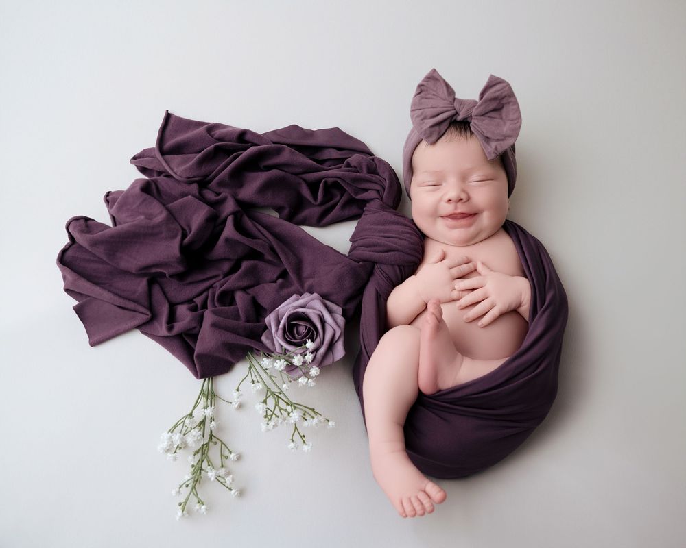 Artistic newborn photography composite showing sleeping baby in plum colored wrap with delicate floral accents.