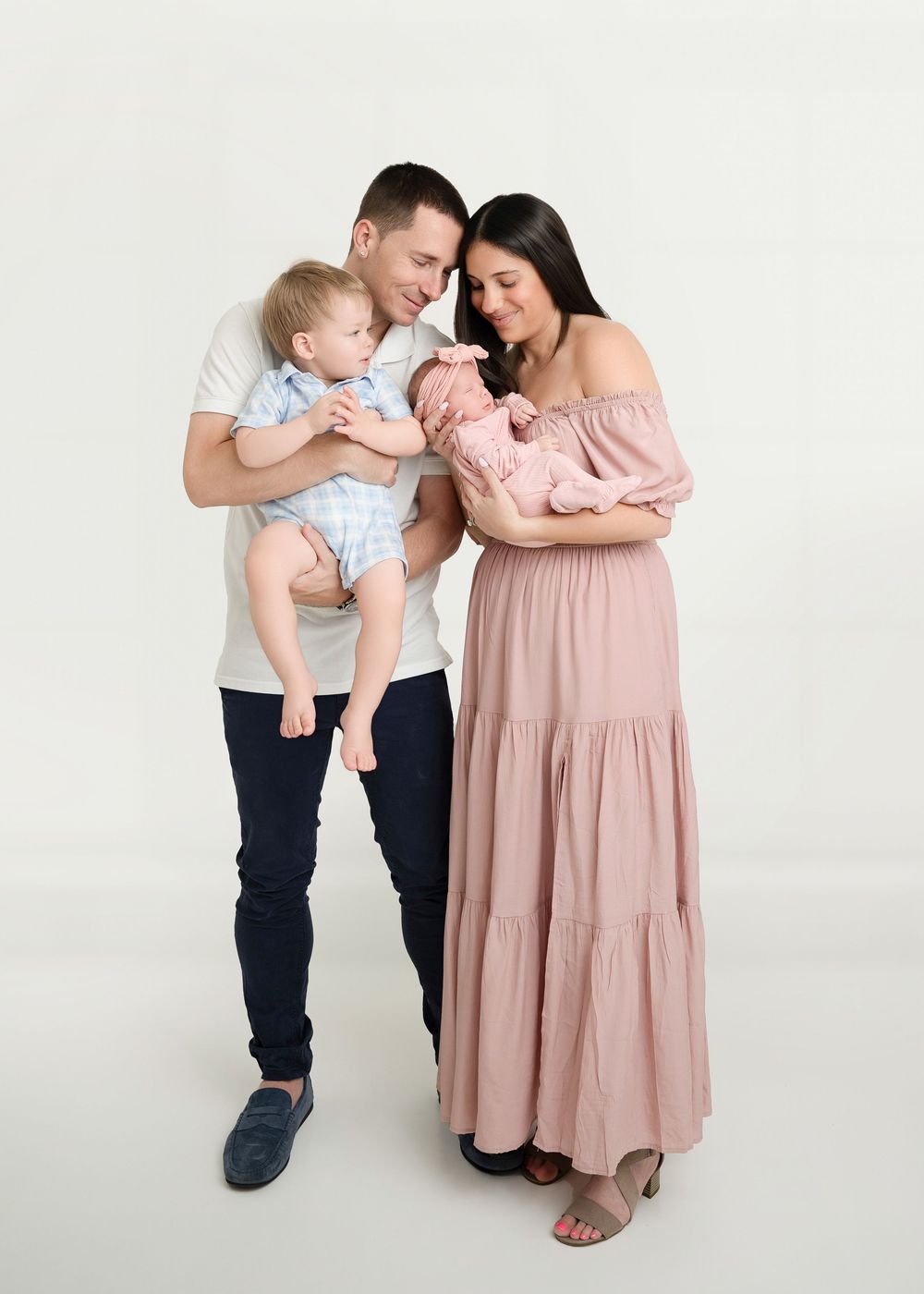Family in coordinated pastel outfits sharing tender moments against white backdrop in studio setting.