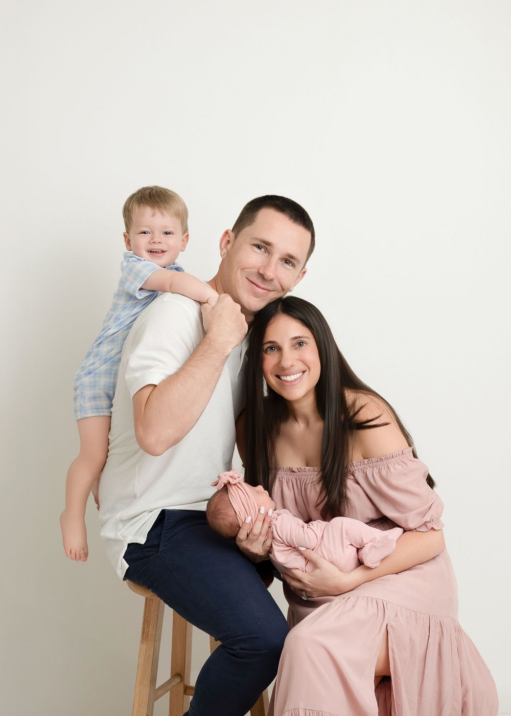 A family in coordinated pink and white outfits poses together for a series of casual studio portraits.