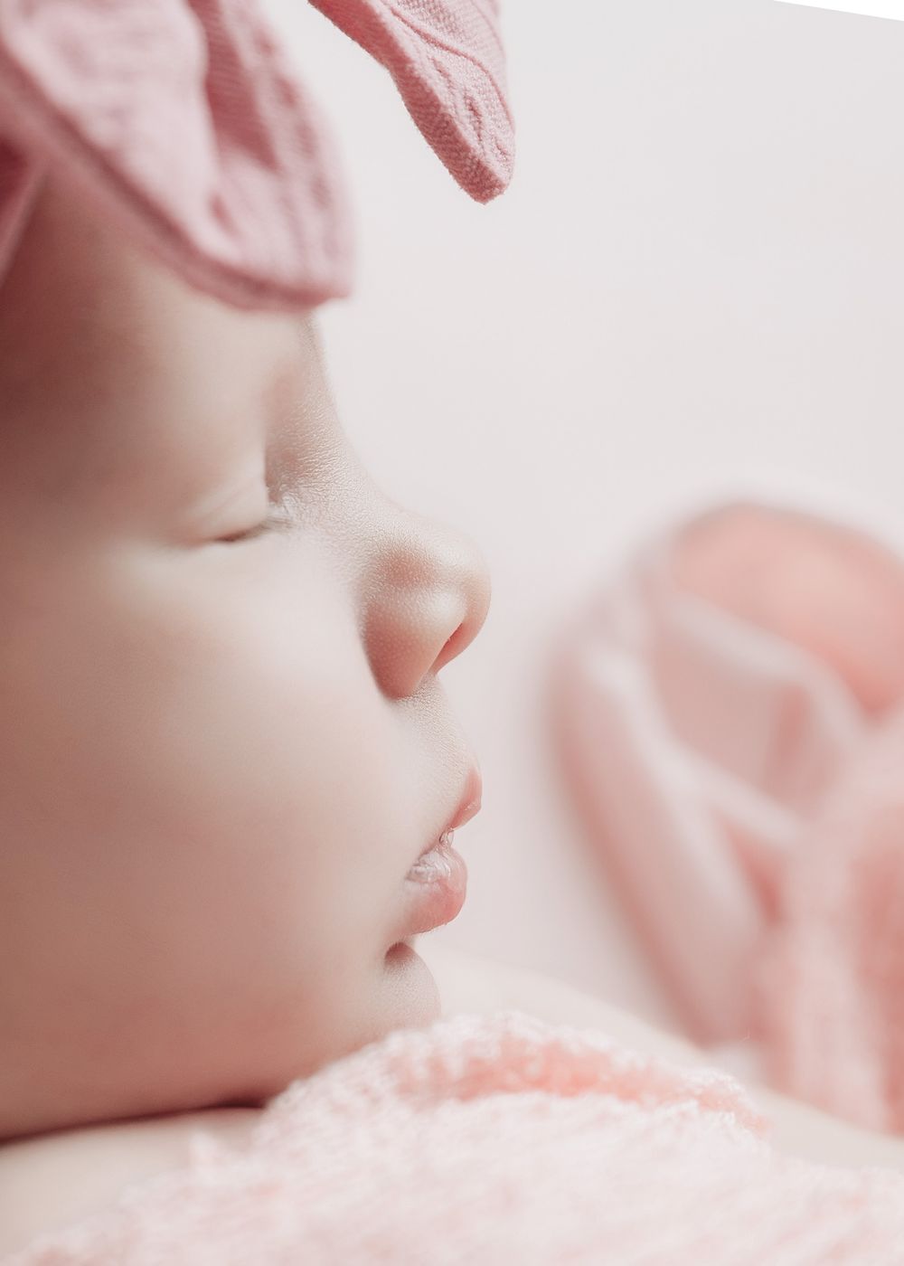 Close-up view of a sleeping baby's face resting on soft pink blanket showing peaceful expression and delicate features.