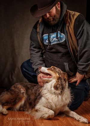 Australian Shepherd dog lying on hardwood floor getting belly rubs from someone wearing a Ford jacket.