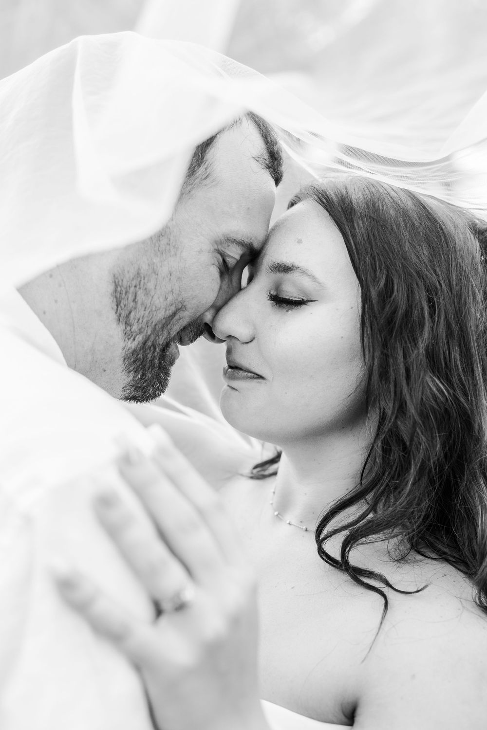 Black and white intimate portrait of a romantic couple in tender embrace with delicate fabric surrounding them.