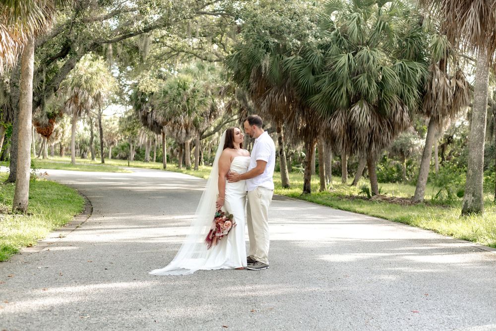 A couple embraces on a palm tree-lined path through a romantic southern park setting during an outdoor wedding.