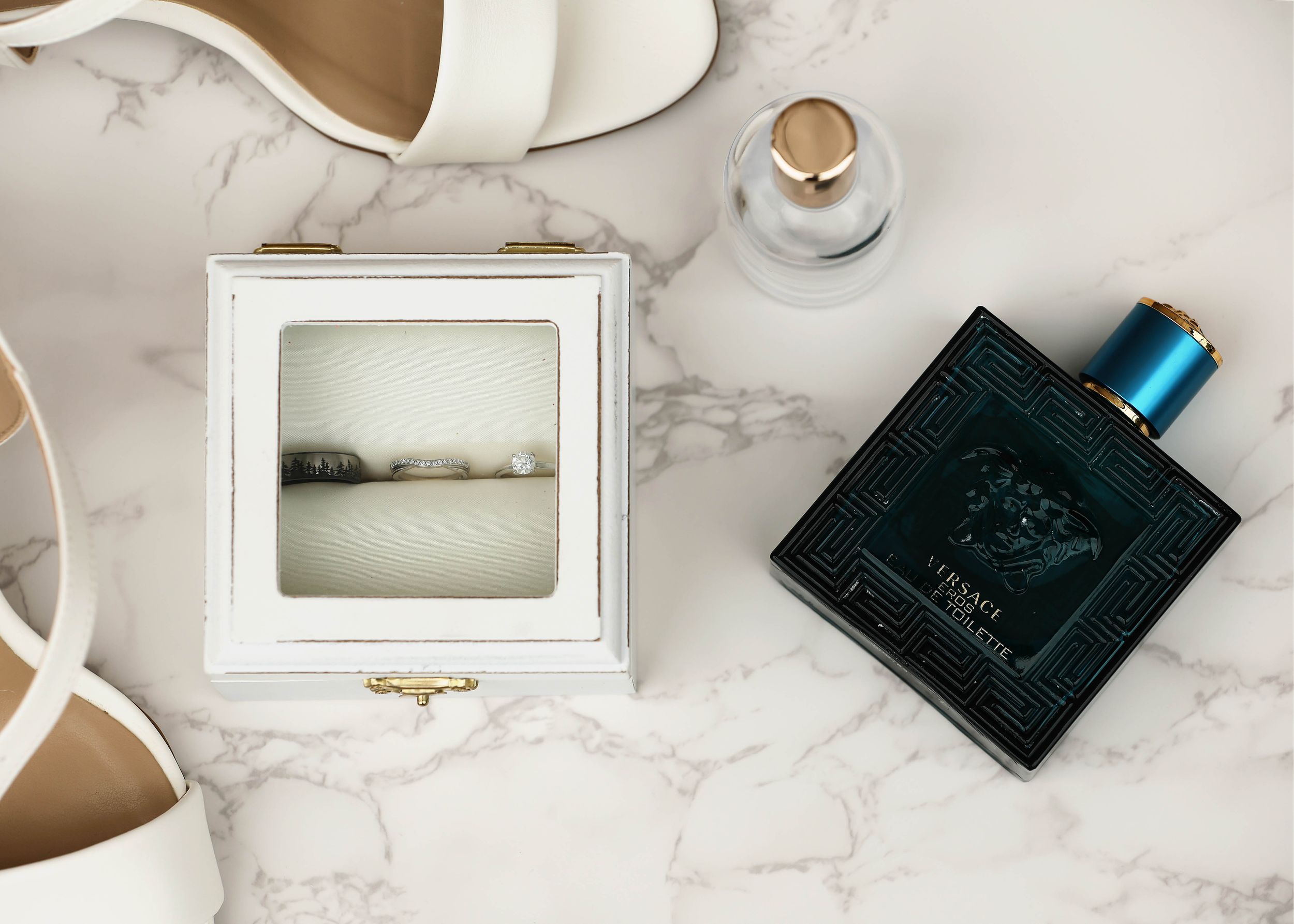 Wedding accessories including perfume bottle and ring box arranged on marble surface.
