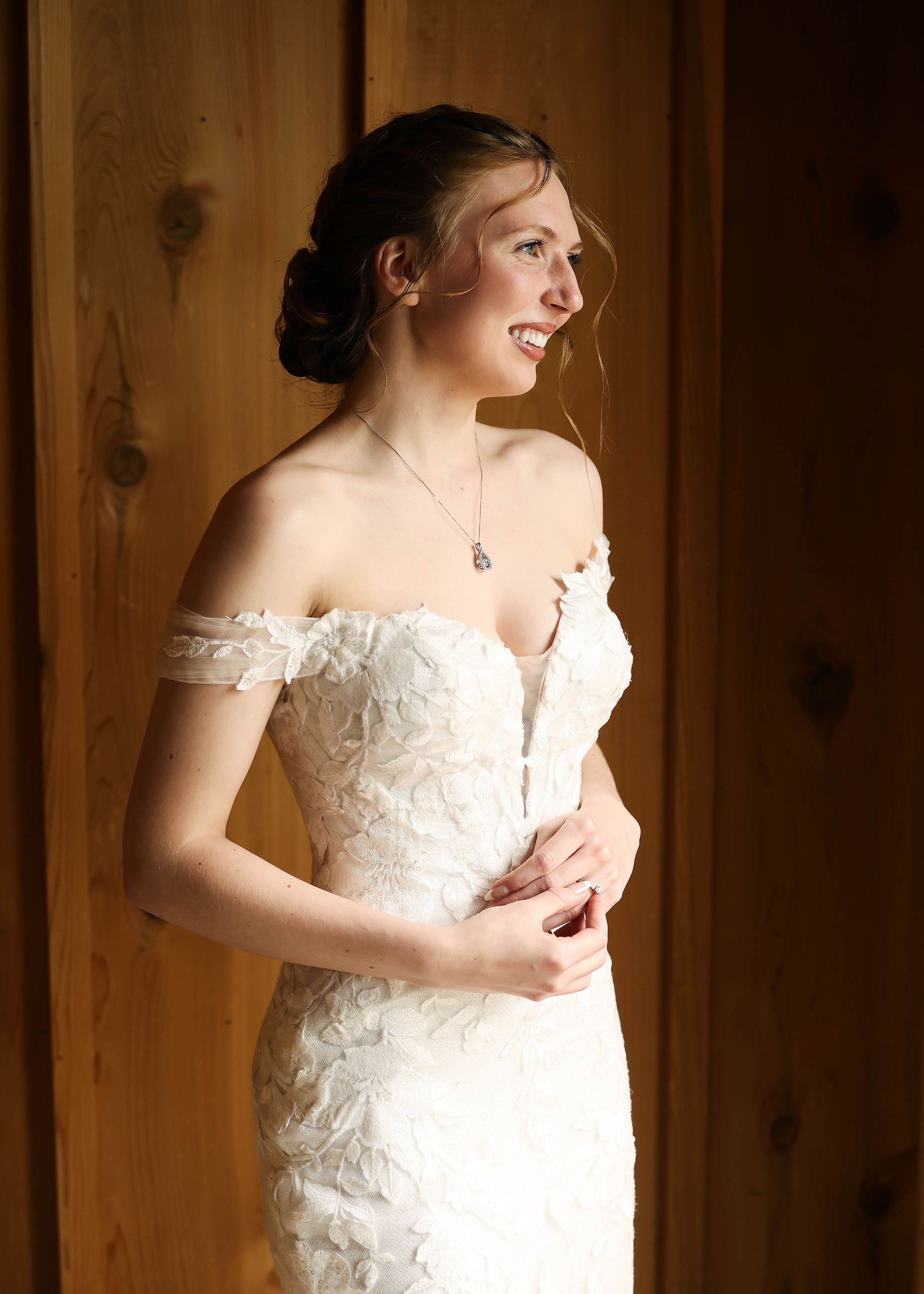 A white lace wedding dress is showcased in a series of detail shots against a wooden wall.