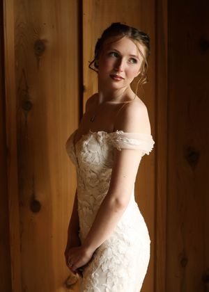 A white wedding dress with delicate lace details is displayed in a rustic wooden setting.