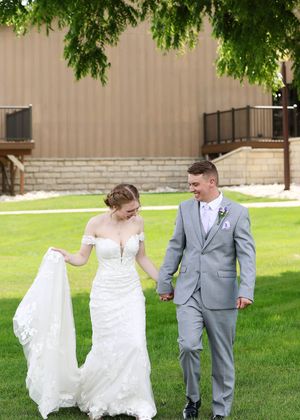A couple playfully walks across a green lawn during their wedding photoshoot.