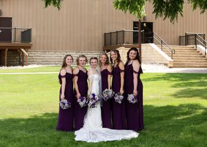 Wedding party in purple bridesmaid dresses posing with bouquets on a sunny lawn.