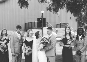 Wedding party in formal attire poses outside a building with stairs.