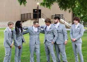Groomsmen in light gray suits share a lighthearted moment outdoors.