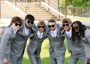 Groomsmen in matching gray suits and sunglasses pose together outdoors.