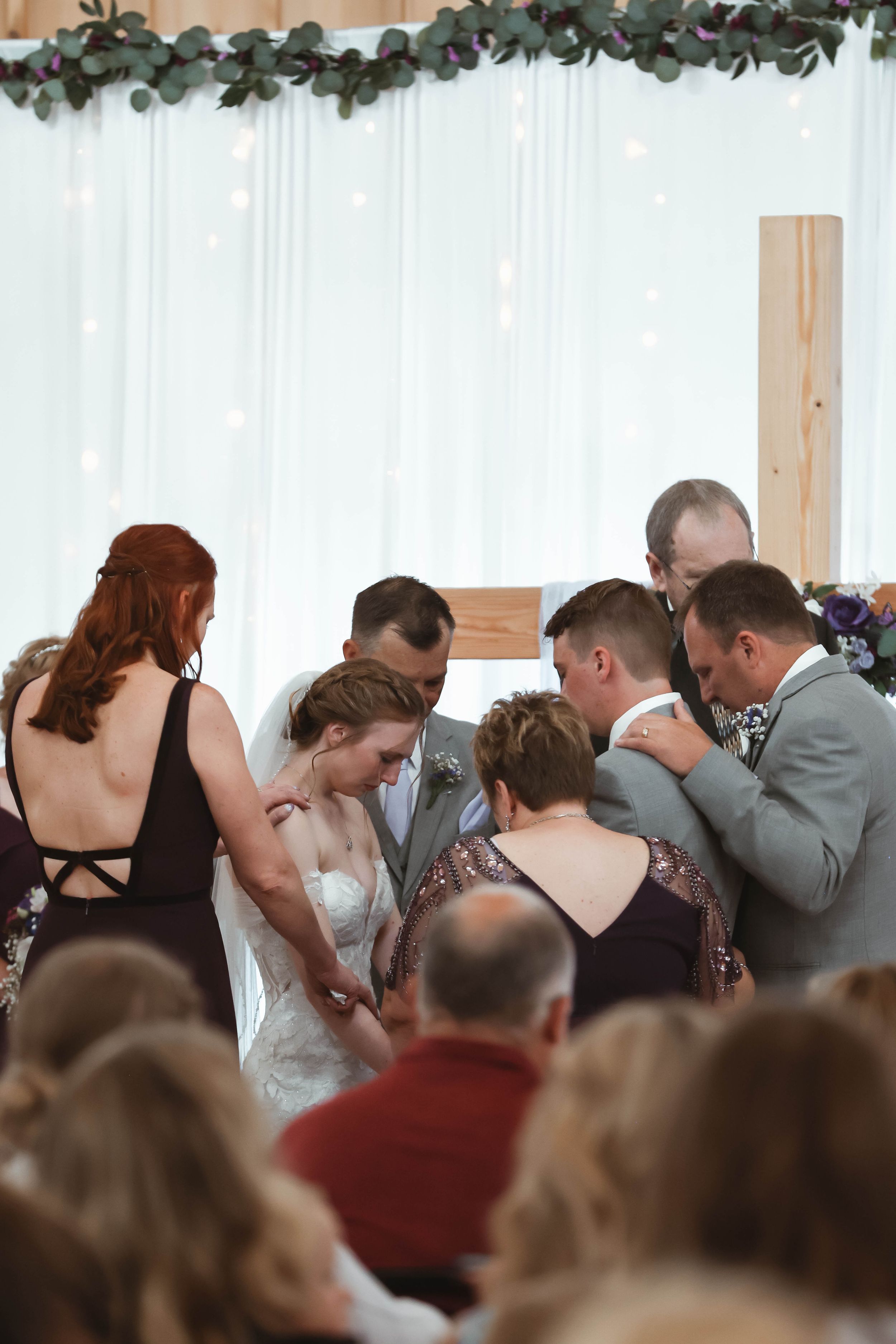 Intimate prayer circle during wedding ceremony under floral arch decor.