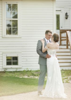 Wedding couple embracing outdoors in front of a white house on their special day.