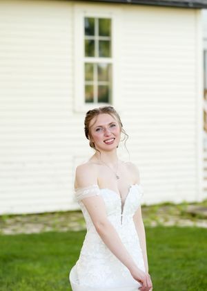 Bride in white off-shoulder gown twirling against white building exterior.