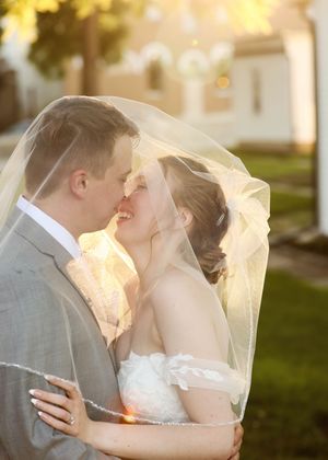 Romantic sunset wedding kiss with bride's veil flowing in golden light.
