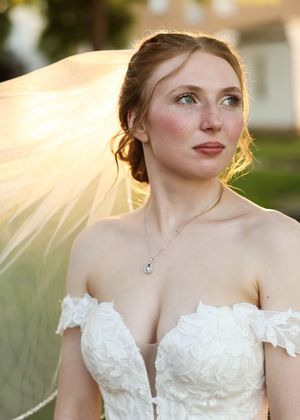 Elegant bridal portrait showcasing off-shoulder lace gown and flowing veil at sunset.