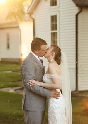 Newlyweds share intimate moments against a white house backdrop during golden hour.